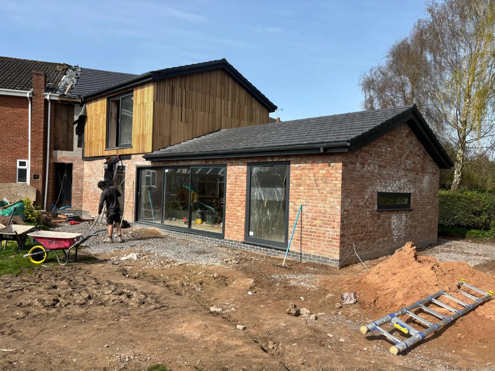 Later stage of the extension with brick walls, timber cladding, roofing and glazing