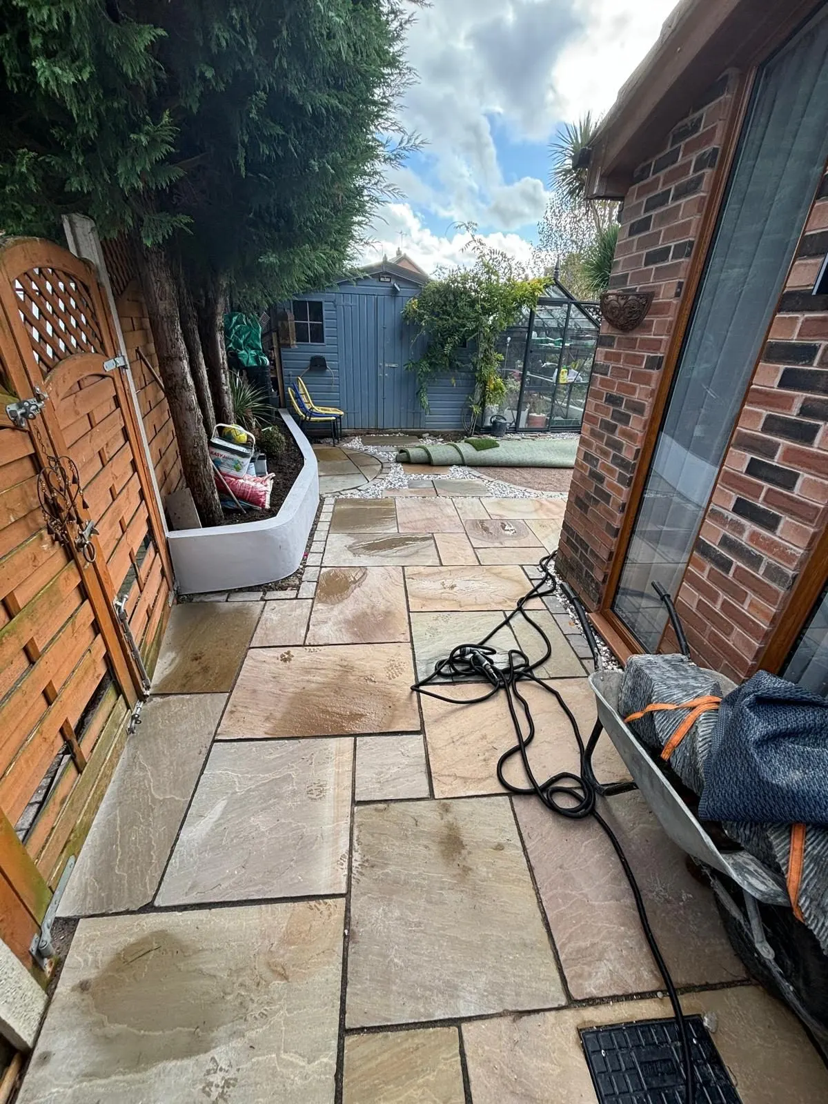 Stone-paved side passage between a brick house and timber fence