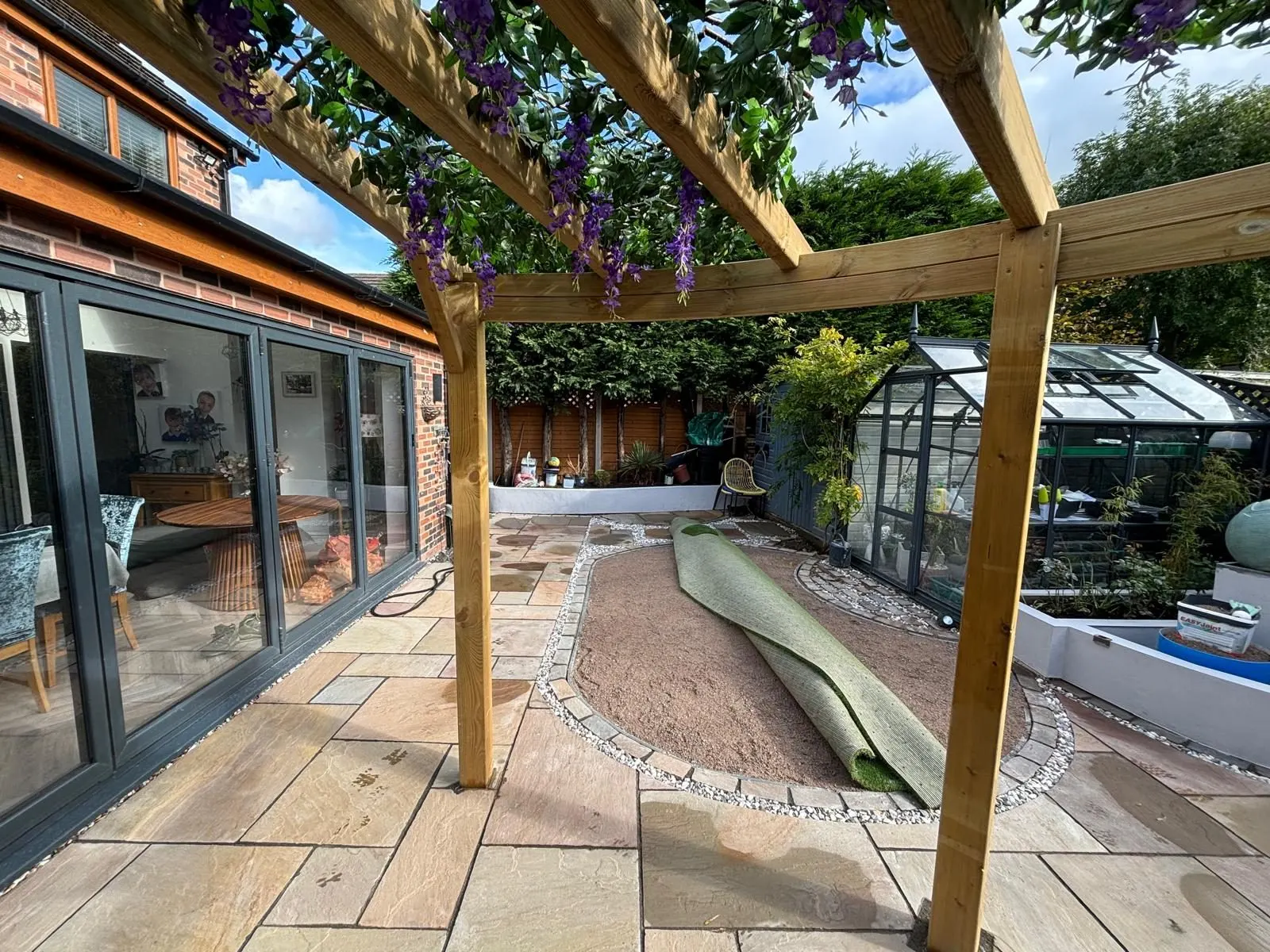 Stone patio beside glazed house doors beneath a timber pergola