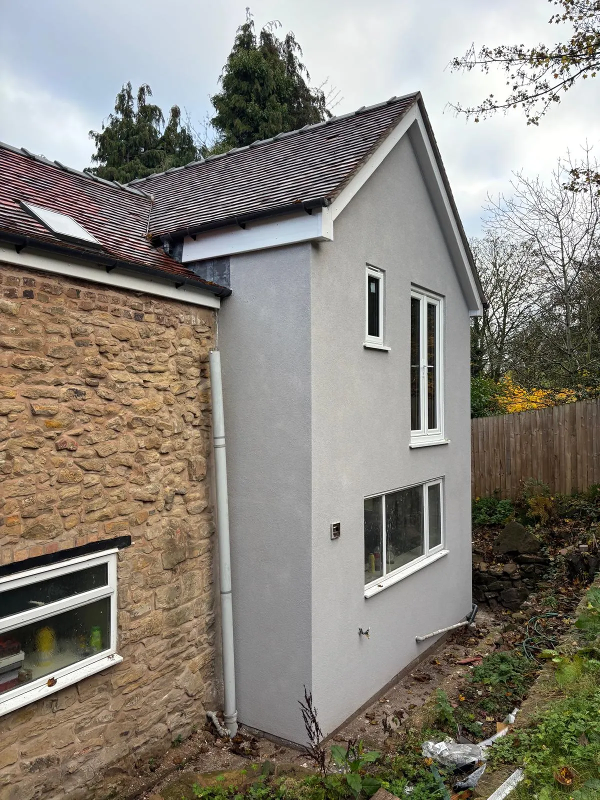Rendered two-storey section adjoining a stone house with a tiled roof